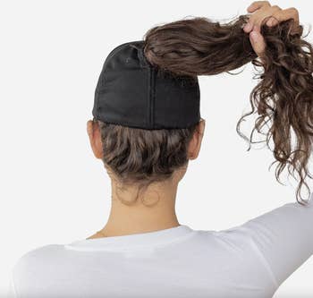 Person pulling hair through the back of a black baseball cap