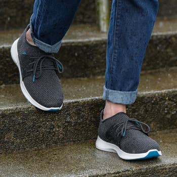 a model wearing the same knit sneakers in dark gray 