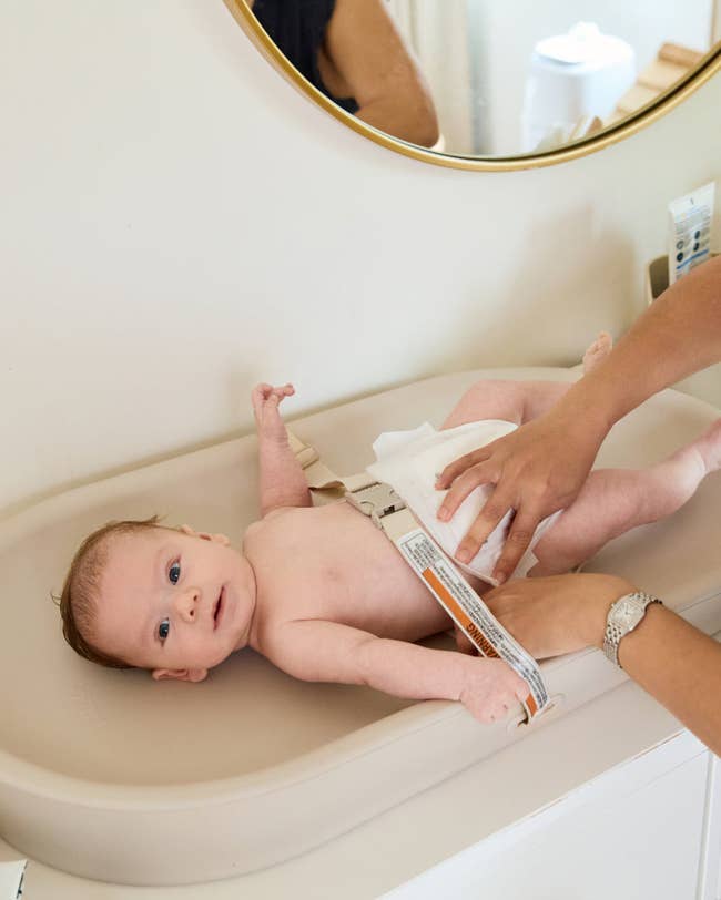 Baby lying connected a changing pad, secured with a strap, portion an big adjusts a diaper successful a location setting