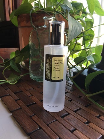 reviewer photo of a bottle of snail mucin essence in front of a window and plant