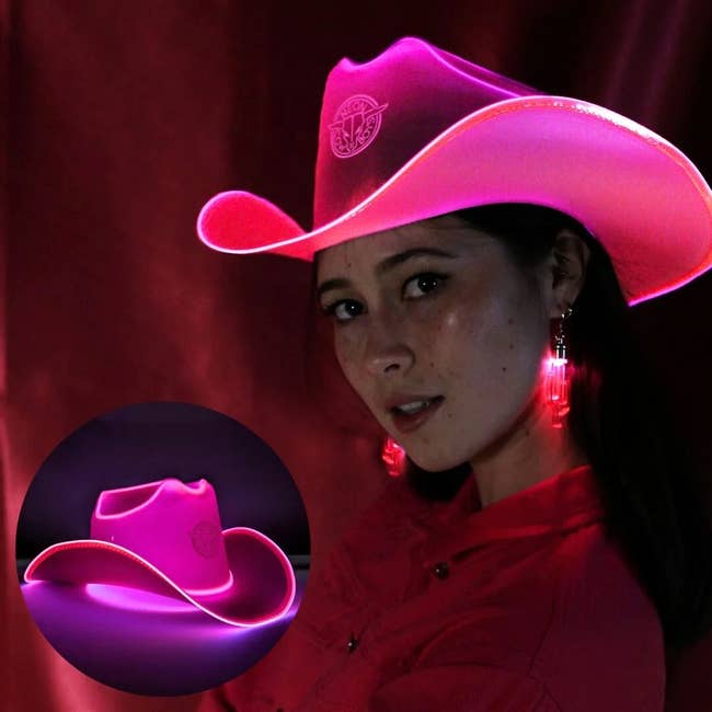 Woman wearing a glowing pink cowboy hat, paired with matching earrings, and a red shirt