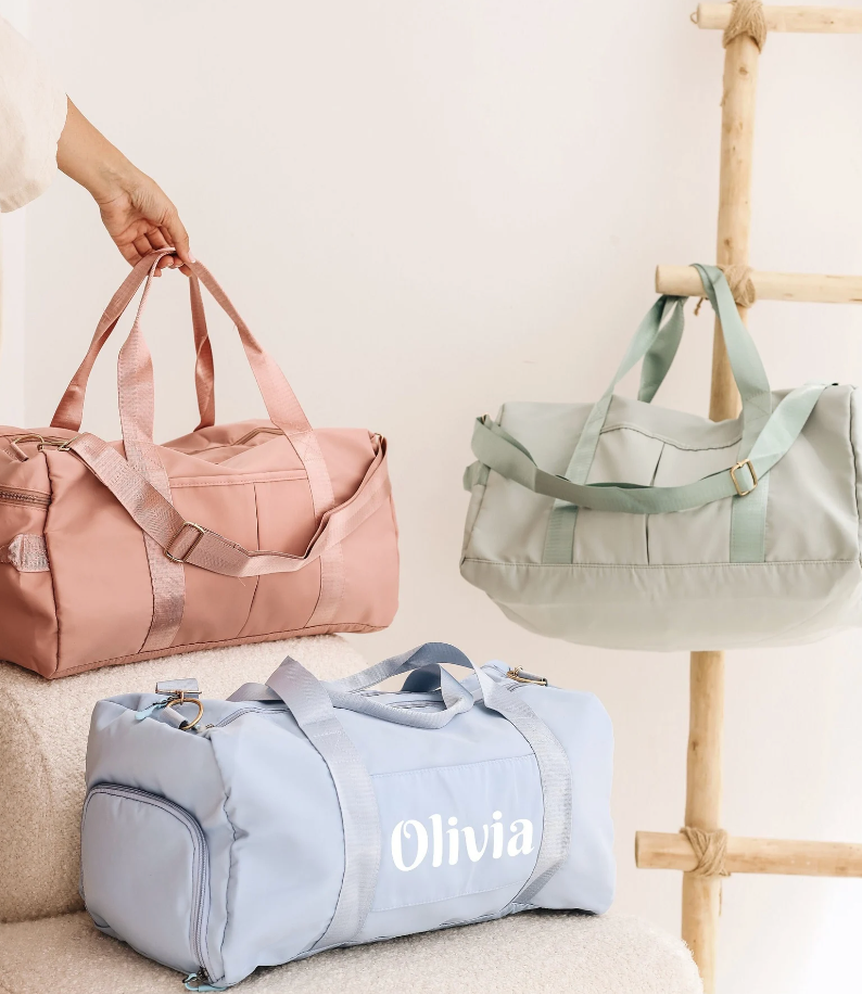 Three duffle bags in pink, green, and blue. The blue one has the name 