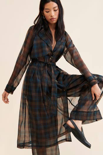 Model in a belted plaid shirtdress and black loafers, posing for a shopping article