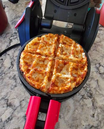 Waffle pizza cooking in a waffle maker on a marble countertop