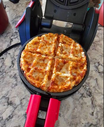 Waffle pizza cooking in a waffle maker on a marble countertop