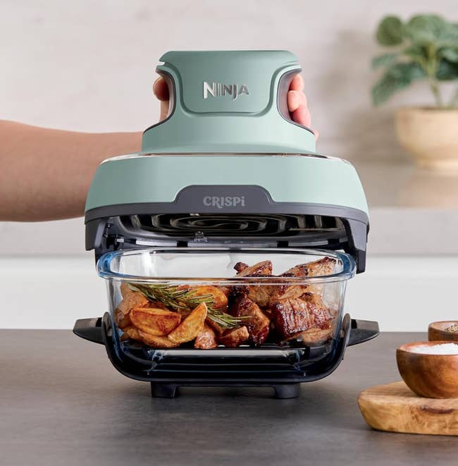 Person utilizing Ninja Crispi aerial  fryer with cooked nutrient   and potatoes wrong  Kitchen mounting  with tableware and plants successful  the background