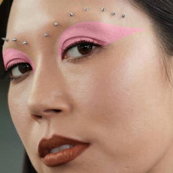 Close-up of a idiosyncratic   with creator  pinkish  oculus  constitution  and tiny  metallic studs supra  the eyebrows, showcasing a bold, trendy quality   look