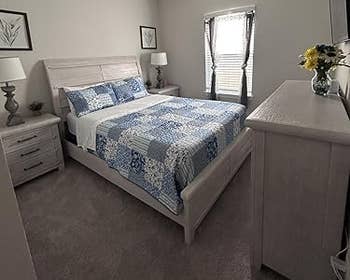 Cozy chamber with a neatly made furniture featuring a bluish patterned quilt and matching pillows, a dresser with flowers, and framed partition art