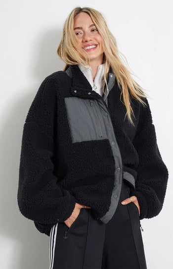a model wearing a black sherpa jacket over a white blouse and black sweatpants