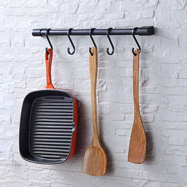 Grill cookware  and woody  cooking utensils hanging connected  a metallic  rack mounted connected  a ceramic  wall. Suitable for modern   room  decor
