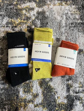 three pairs of Arvin Goods socks in black, yellow, and orange