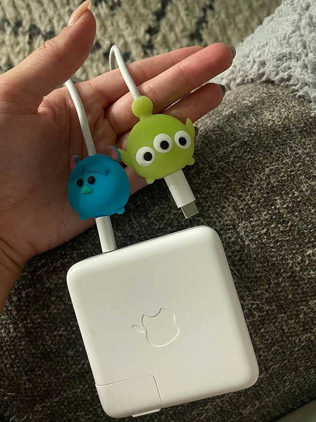 Hand holding Apple charger with blue and green alien cartoon cable protectors