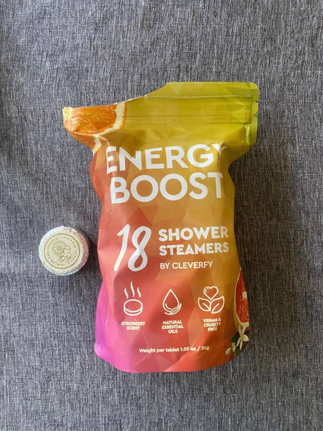 Package of Energy Boost Shower Steamers with a citrus design, placed on a fabric surface, next to a small cap