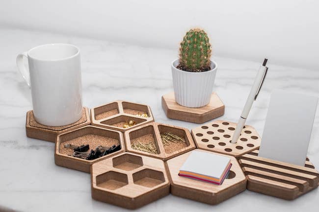 nine hexagon-shaped organizers on a desk filled with paperclips, pens, post-its, and a mug.