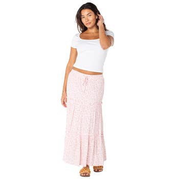 Woman in a casual white top and floral long skirt poses, showcasing a relaxed summer outfit, suitable for a shopping-themed article
