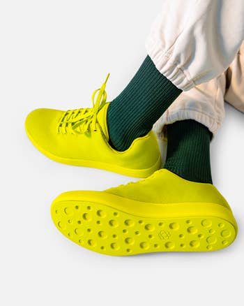 Yellow sneakers with textured soles worn with acheronian  greenish  socks and achromatic  pants
