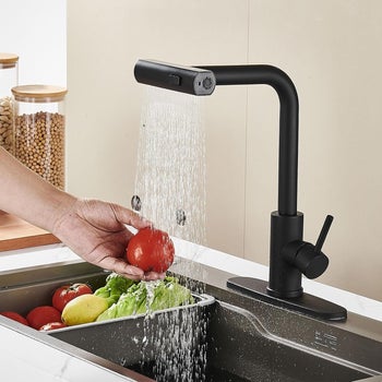 model washing vegetables under a modern black kitchen faucet with spray feature