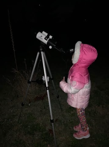 reviewer's child in winter coat with hood looking through telescope