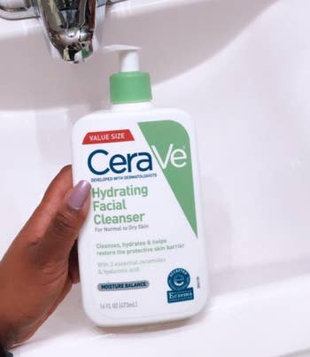 reviewer holding the white and green cleanser bottle