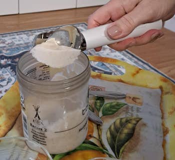 Person scooping creamy substance   from a jar onto a decorative tray with beverage  utensils