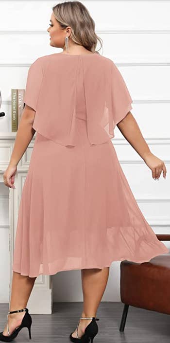 same model wearing the dress in pink showing the cape from the back