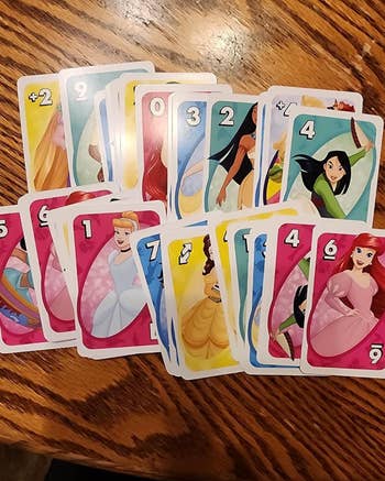 Playing cards featuring assorted  animated princesses are dispersed  retired  connected  a woody  table