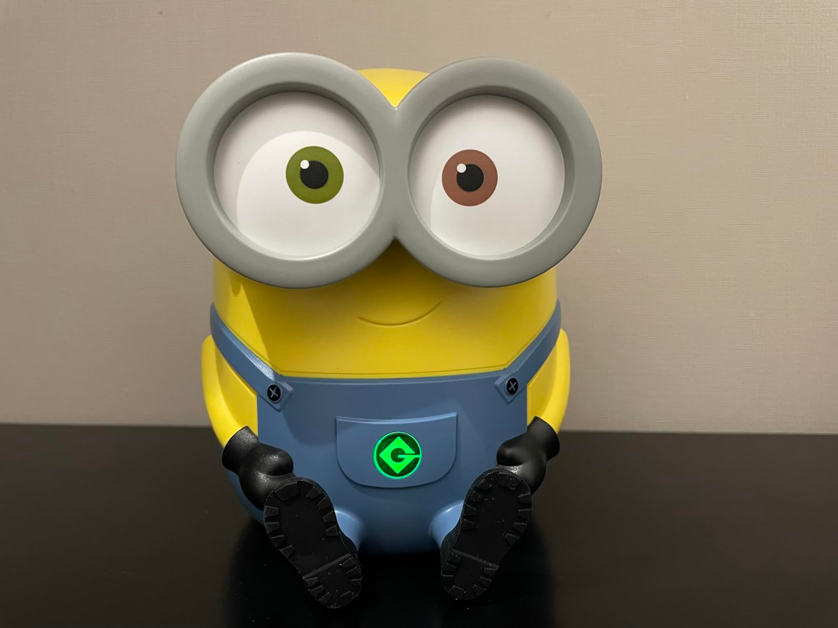 A toy resembling a Minion with large goggles and a G logo on its overalls, sitting on a flat surface