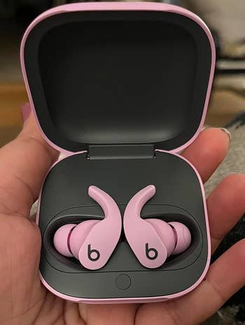 Pink wireless earbuds in an open charging case held in a hand, suitable for fitness and active use