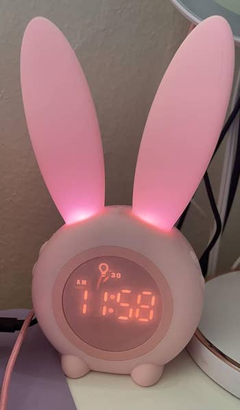 small glowing pink digital alarm clock with glowing bunny ears 