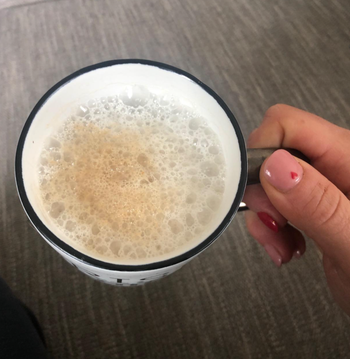 A reviewer holding a frothy creamy cup of coffee 