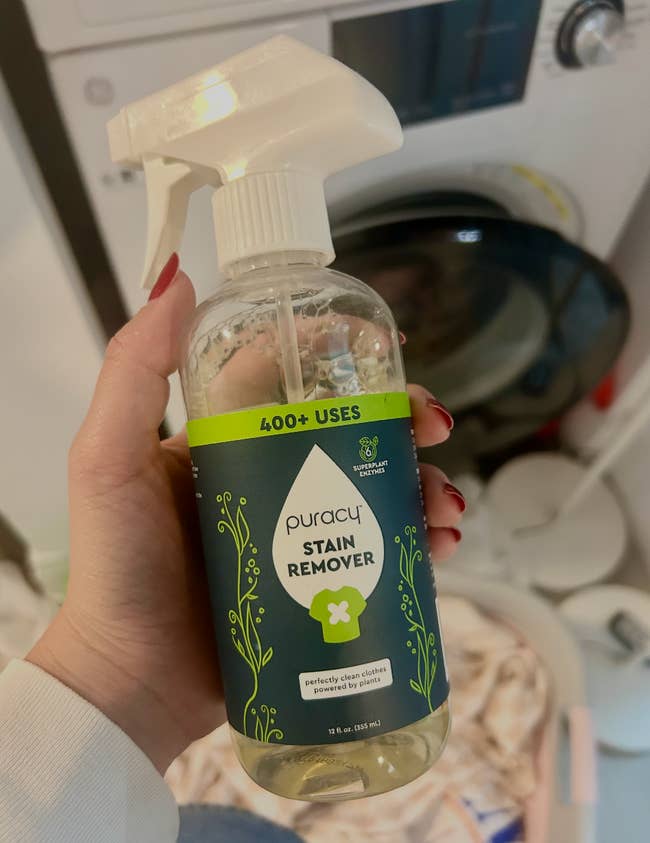 Hand holding a vessel of Puracy Stain Remover with a washing instrumentality successful the background. The statement notes
