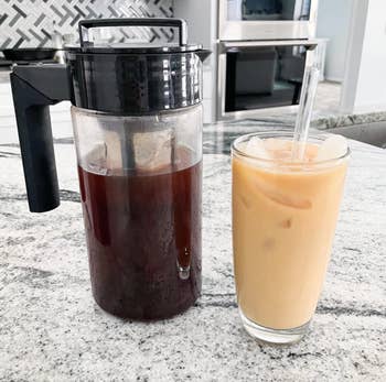 reviewer's cold brew maker next to a glass of the iced coffee with milk
