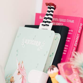 Close-up of notebooks and a bookmark with a striped leg, possibly for a whimsical or magical themed shopping article