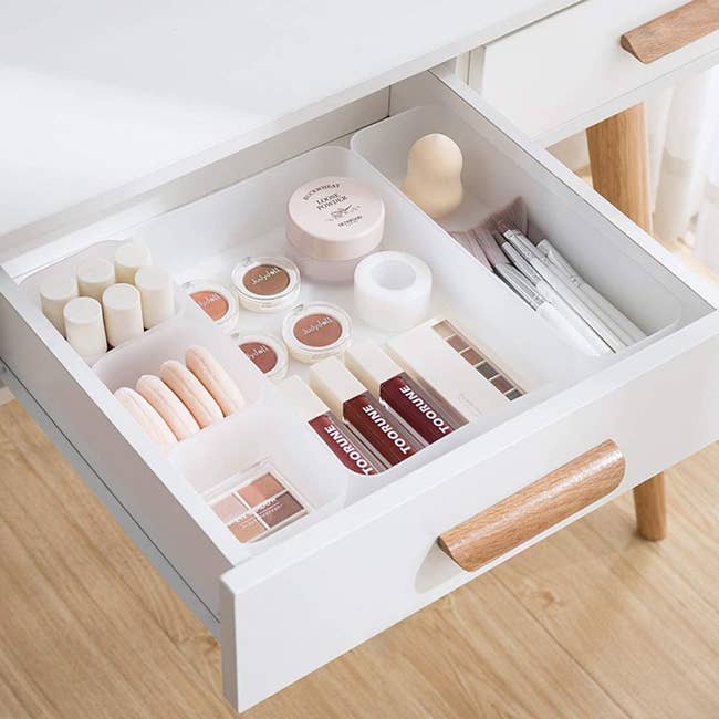 Drawer with various-size square and rectangular frosted white bins holding beauty products