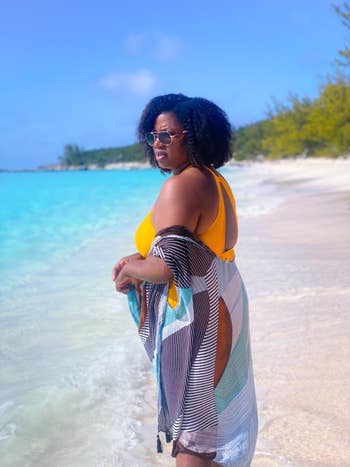 Woman in a yellow swimsuit and striped cover-up stands on a beach