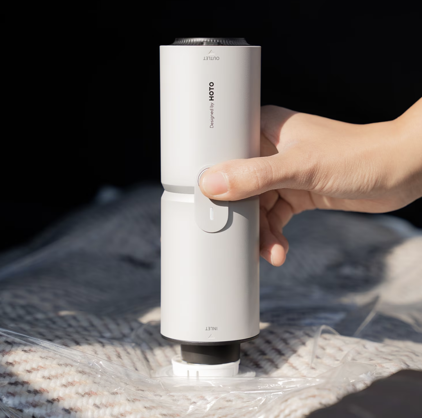 Hand utilizing a portable vacuum sealer connected  a plastic-covered blanket, demonstrating its functionality and easiness  of use