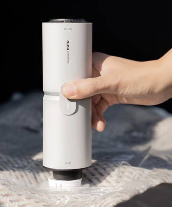Hand utilizing a portable vacuum sealer connected a plastic-covered blanket, demonstrating its functionality and easiness of use