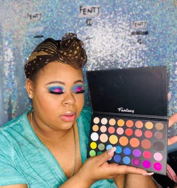A reviewer holding up the makeup palette with eyeshadow on their face
