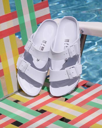 White sandals with buckles on a striped pool chair by water