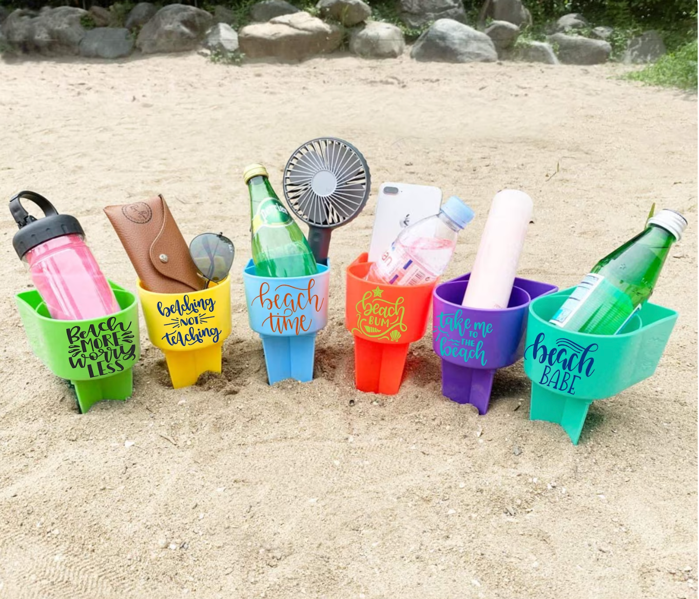 different colors of plastic holders with stakes leveling them in the sand and drinks and phones in their compartments 