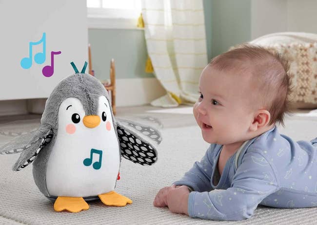 Baby on tummy facing a musical penguin toy in a nursery setting.