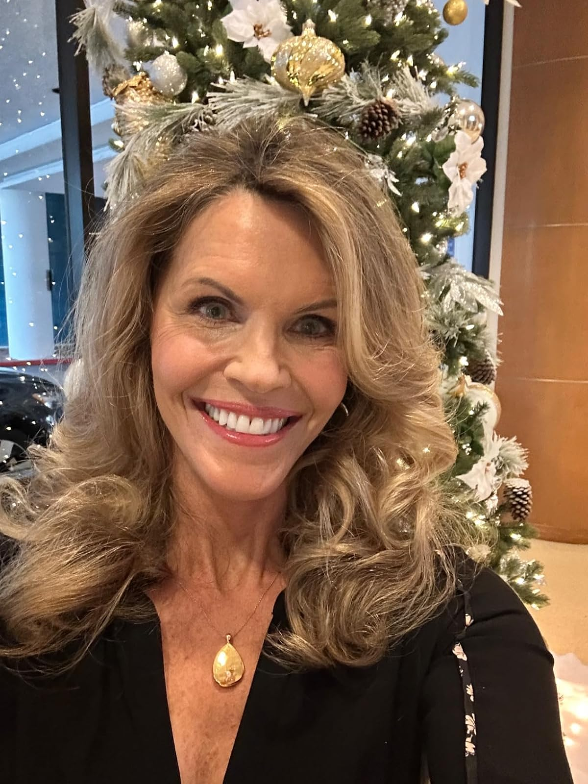 Person smiling successful  beforehand   of a decorated Christmas tree, wearing a achromatic  apical  with a golden  pendant necklace