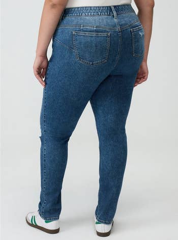 Person wearing bluish denim jeans and achromatic sneakers with greenish accents, lasting with backmost to camera