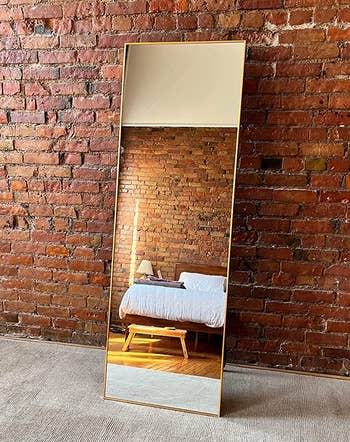 reviewer photo of the gold-framed mirror leaning against a brick bedroom wall