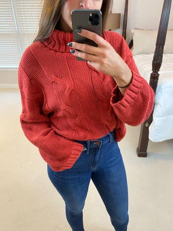 reviewer photograph  of them wearing a reddish  turtleneck sweater with bluish  jeans
