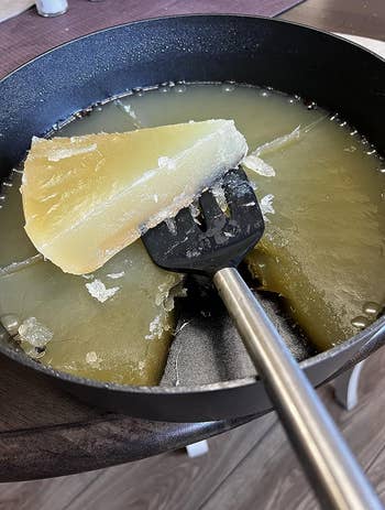 reviewer using a spatula to remove the solidified oil from a pan
