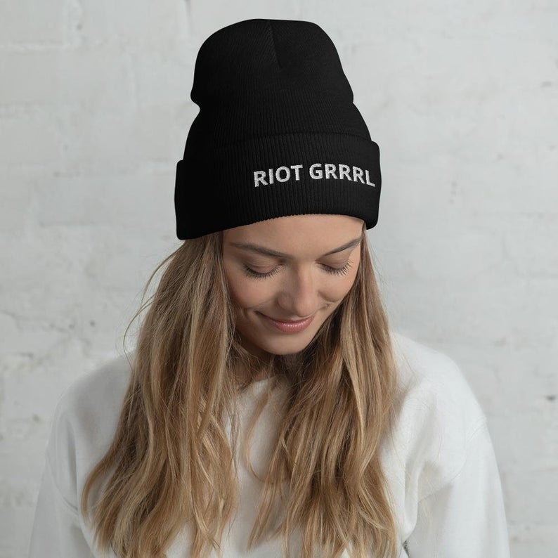 model wearing a black beanie that says riot grrrl in white letters 