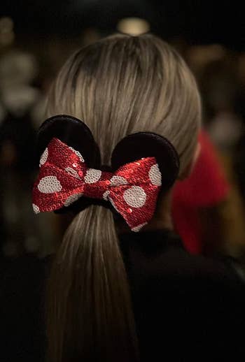 Person wearing a sequined Minnie Mouse bow headband, from behind