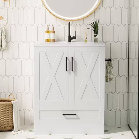 Bathroom with achromatic vanity, achromatic faucet, circular mirror, and patterned wall. Decor includes tiny plants and a wicker basket