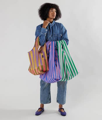 a model holding the three shopping bags featuring different colored stripe prints 